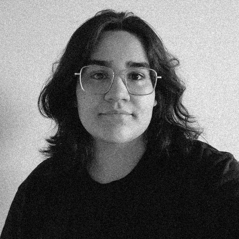 Retrato fotográfico em preto e branco de uma pessoa jovem, apresentado dentro de uma moldura circular. Ela tem cabelos escuros, de comprimento médio e levemente ondulados, que emolduram o rosto. Usa óculos de grau com armação metálica fina e retangular. Veste uma camiseta escura e olha diretamente para a câmera com uma expressão tranquila. A imagem mantém a estética de textura granulada e alto contraste, semelhante a uma impressão em papel jornal ou estêncil, comum aos outros retratos da série. O círculo está centralizado sobre um fundo branco com texturas sutis.