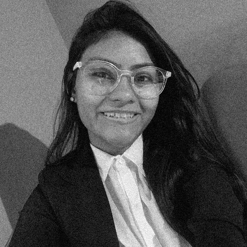 Retrato fotográfico em preto e branco de uma mulher jovem, apresentado dentro de uma moldura circular. Ela tem cabelos escuros e longos, e usa óculos de grau com armação clara e arredondada. Ela sorri para a câmera, transmitindo uma expressão amigável. Veste uma camisa social clara por baixo de um blazer escuro. A imagem mantém a estética de alto contraste e textura granulada, como se fosse uma impressão em papel jornal ou estêncil. O círculo está centralizado sobre um fundo branco com texturas sutis que lembram papel.