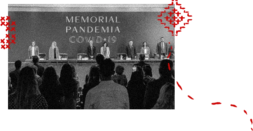 Fotografia em preto e branco de um evento institucional. No palco, um grupo de pessoas está de pé atrás de uma mesa, diante de um painel com o texto “Memorial Pandemia COVID-19”. Em primeiro plano, há uma plateia vista de costas. Elementos gráficos em vermelho, como pequenos “X” e traços pontilhados, aparecem sobrepostos nas laterais da imagem, criando contraste com a cena.